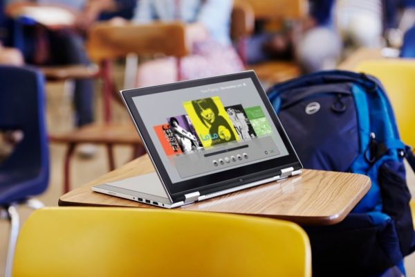 Dell Inspiron 11 3000 Series 2-in-1 Touch (Model 3147) notebook computer in tablet position (with keyboard serving as stand), on a student desk in a classroom, with Dell Energy backpack in seat and blurry students in background.